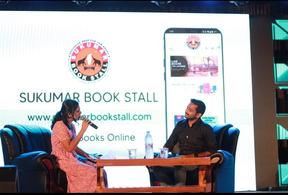 Sukumar Book Stall's online store shown on the stage screen behind an interview with Basil Joseph